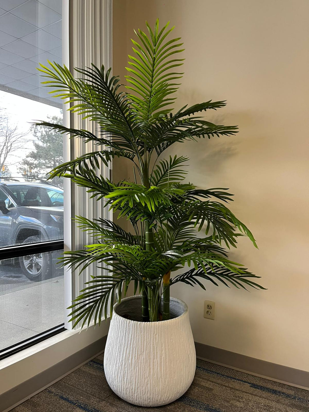Large white textured planter holding a lush green artificial palm tree, placed near a window with natural light. The planter's modern ribbed design complements the vibrant greenery. Is the planter suitable for both artificial and live plants?