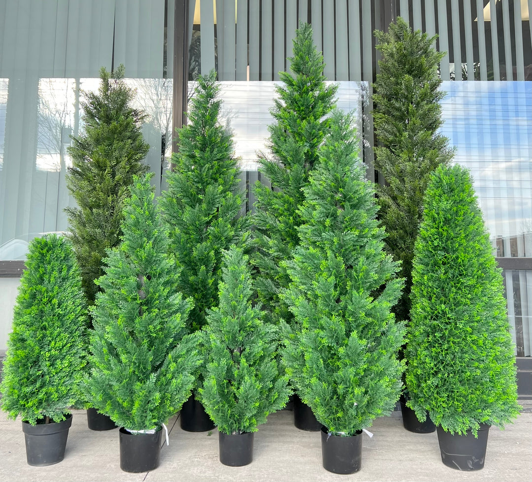 Collection of artificial evergreen trees in varying sizes, all potted in black containers, arranged outdoors against a window, ideal for creating a lush, natural ambiance in any setting.