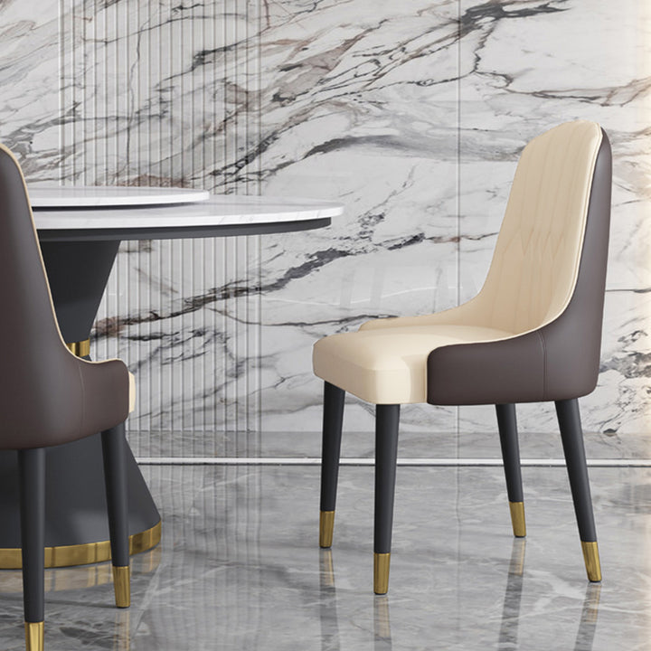 A luxurious beige and brown upholstered dining chair with black legs and gold-capped feet, paired with a marble-topped dining table set against a marble wall backdrop. Frequently asked questions might include 'What are the best materials for an elegant dining chair?' and 'How do you choose chairs that complement a marble dining table?