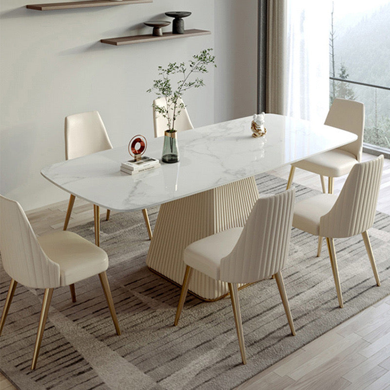 Rectangular marble dining table with a modern fluted base, surrounded by six cream upholstered chairs with gold legs, set in a stylish dining room with minimalist decor.