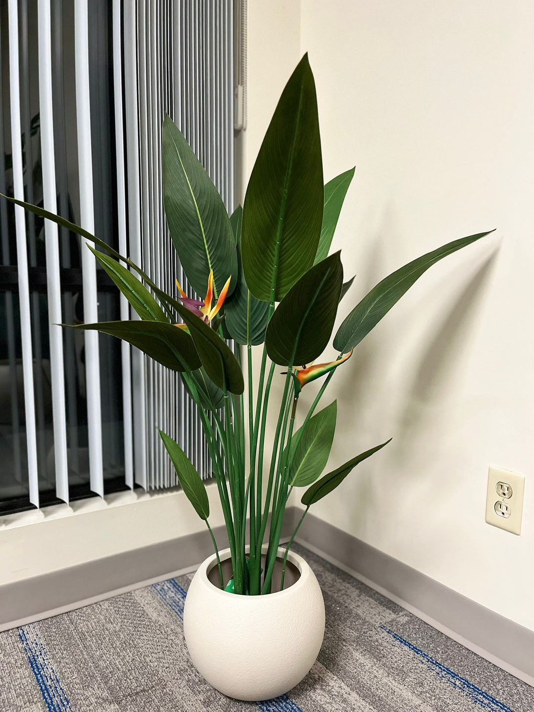 Ivory round planter with a smooth matte finish, holding a vibrant artificial bird of paradise plant with broad green leaves and colorful flowers, placed indoors near a window. Does this planter come with a protective inner lining?