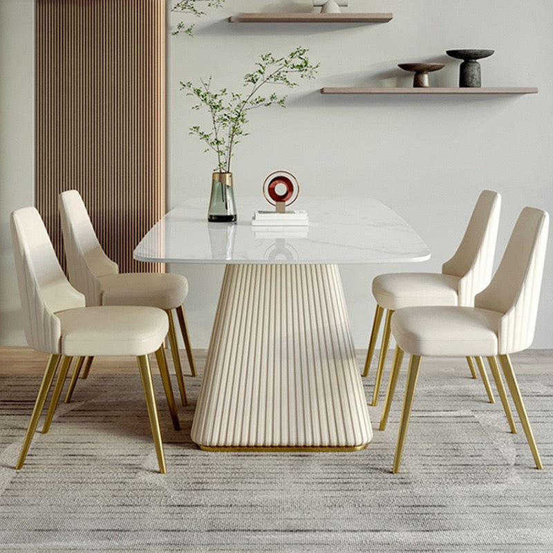 Contemporary dining room setup with a rectangular marble table featuring a fluted base, surrounded by six cream upholstered chairs with gold legs, set against a minimalist backdrop with modern decor elements