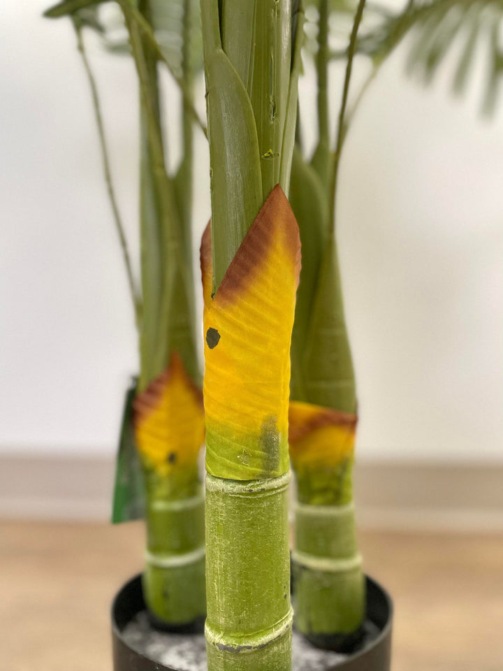 Close-up of a palm tree's artificial trunk, displaying green stems with yellow and brown accents at the base. The detail highlights the textured and realistic design of the tree.