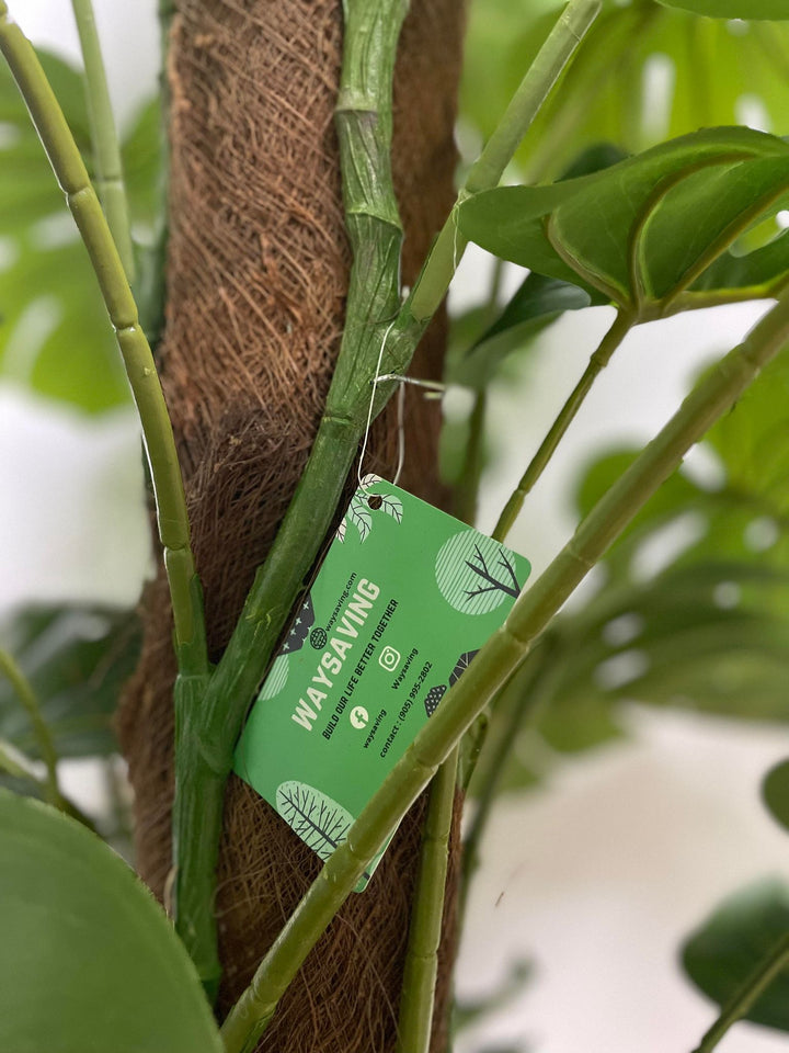 Close-up of a tag attached to an artificial Monstera plant's stem. What are the benefits of artificial plants for indoor spaces?