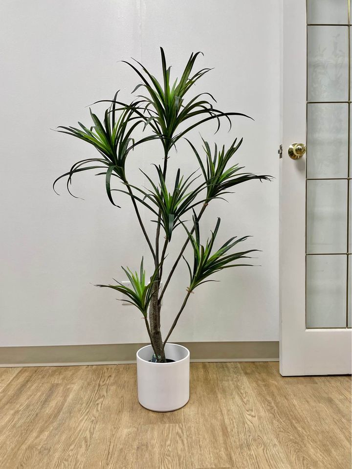 Artificial yucca tree in a white planter placed against a white wall and wooden floor, perfect for indoor home or office decor