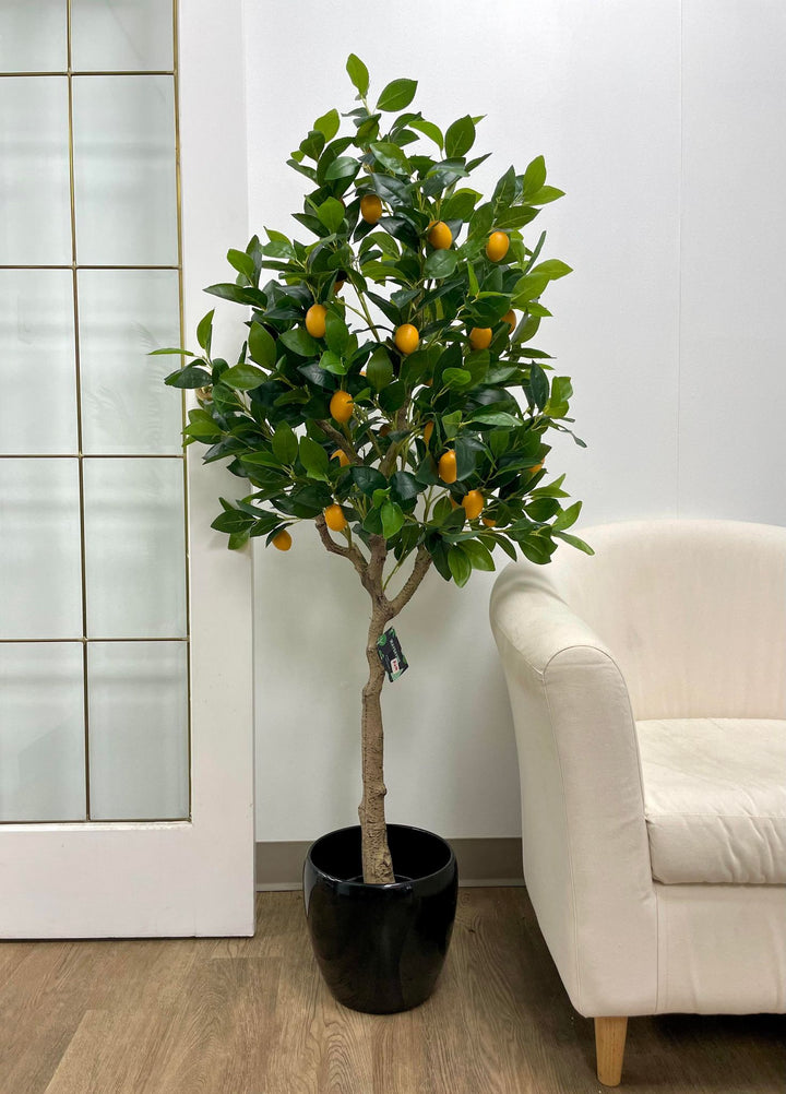 Artificial lemon tree with lush green leaves and bright yellow lemons in a tall black planter, placed near a glass-paneled door in a modern indoor setting