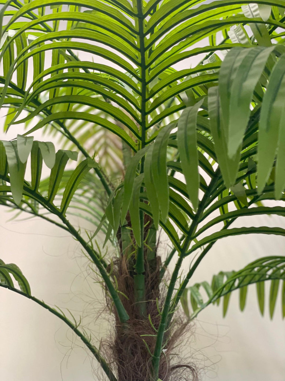 Close-up view of an artificial palm tree, showcasing realistic green fronds and detailed textured trunk with natural-looking fibers.