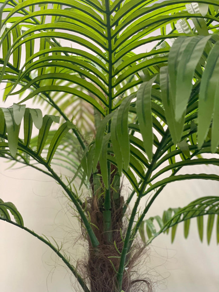 Close-up view of an artificial palm tree, showcasing realistic green fronds and detailed textured trunk with natural-looking fibers.