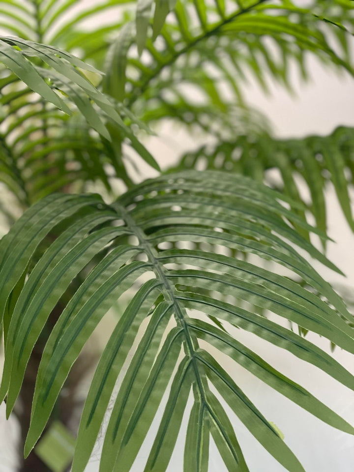 Close-up of vibrant green artificial palm leaves, showcasing their detailed texture and lush tropical aesthetic, perfect for enhancing indoor decor with a natural touch.