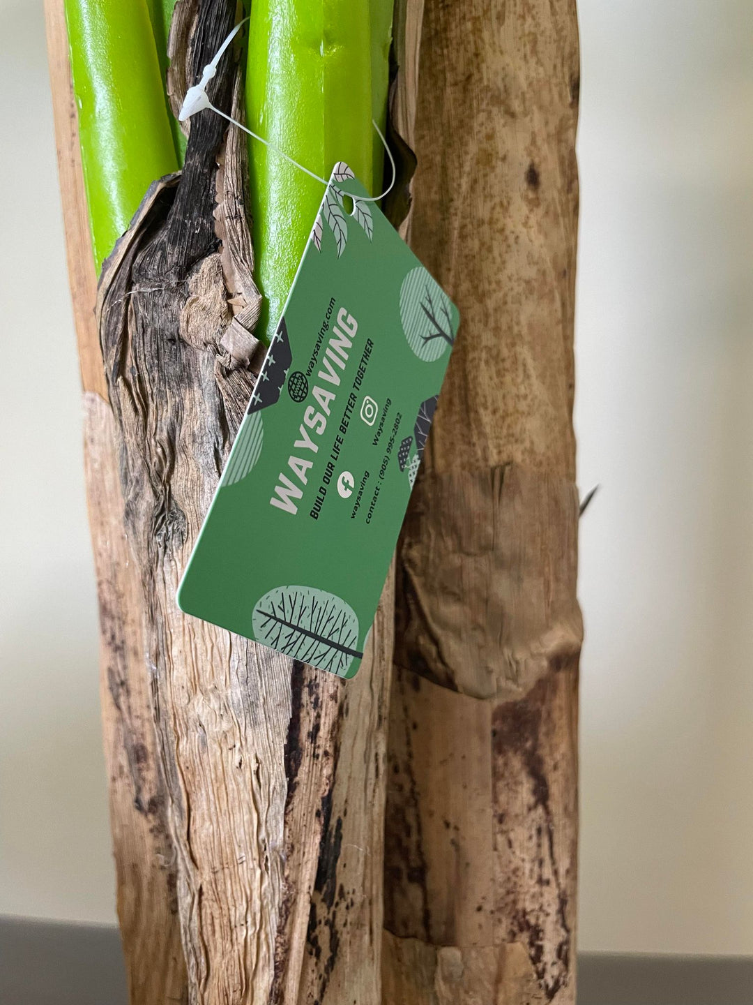 Close-up of an artificial banana plant trunk with a green tag labeled 'WAYSAVING,' highlighting the realistic texture and quality of the plant's materials