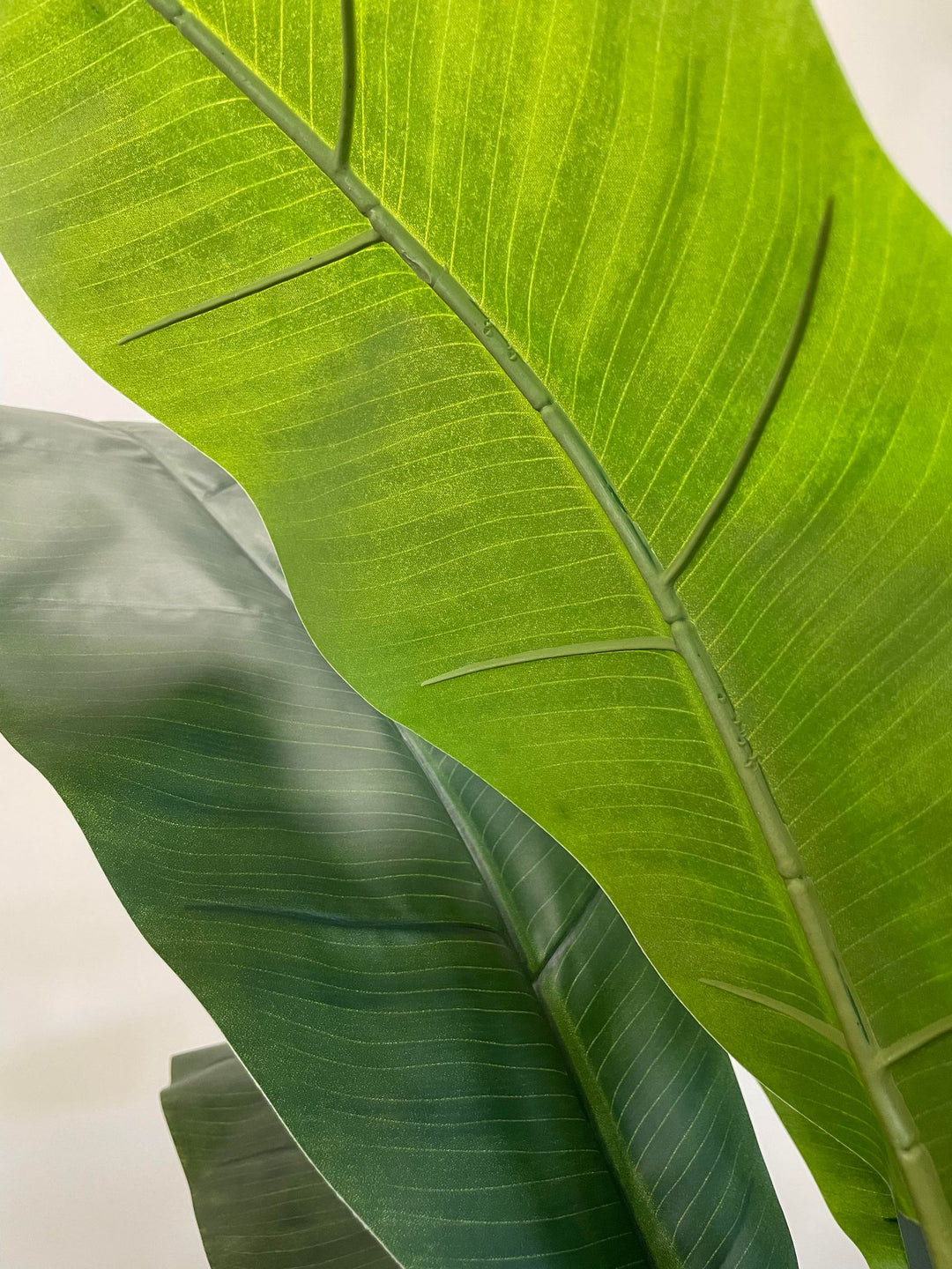 Close-up view of vibrant green artificial banana leaves, showcasing detailed texture and realistic veining, perfect for enhancing indoor spaces with a natural look.
