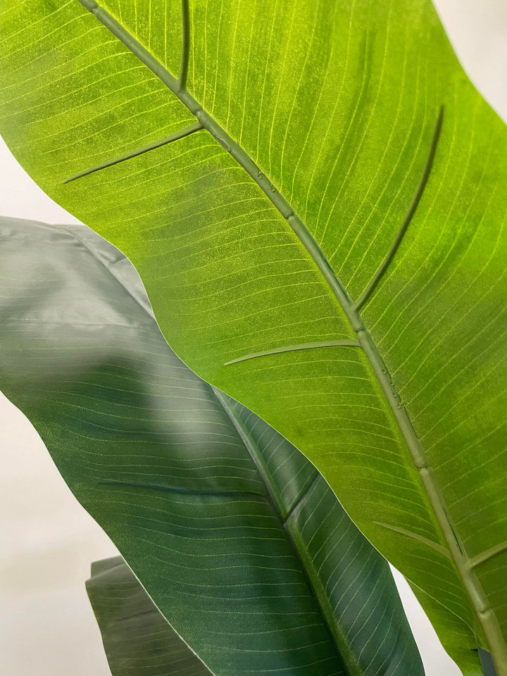 Close-up view of vibrant green artificial banana leaves, showcasing detailed texture and realistic veining, perfect for enhancing indoor spaces with a natural look.