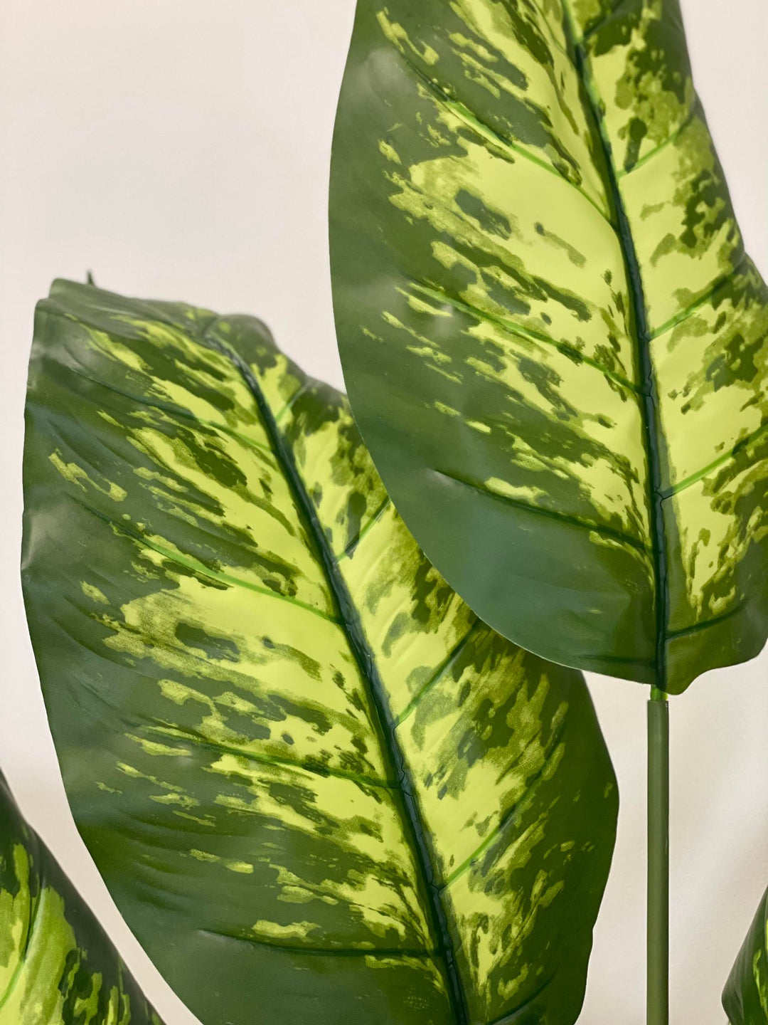 Close-up of the vibrant, variegated leaves of a tall artificial plant, showcasing the intricate patterns of green and yellow, adding a touch of natural beauty to the space.