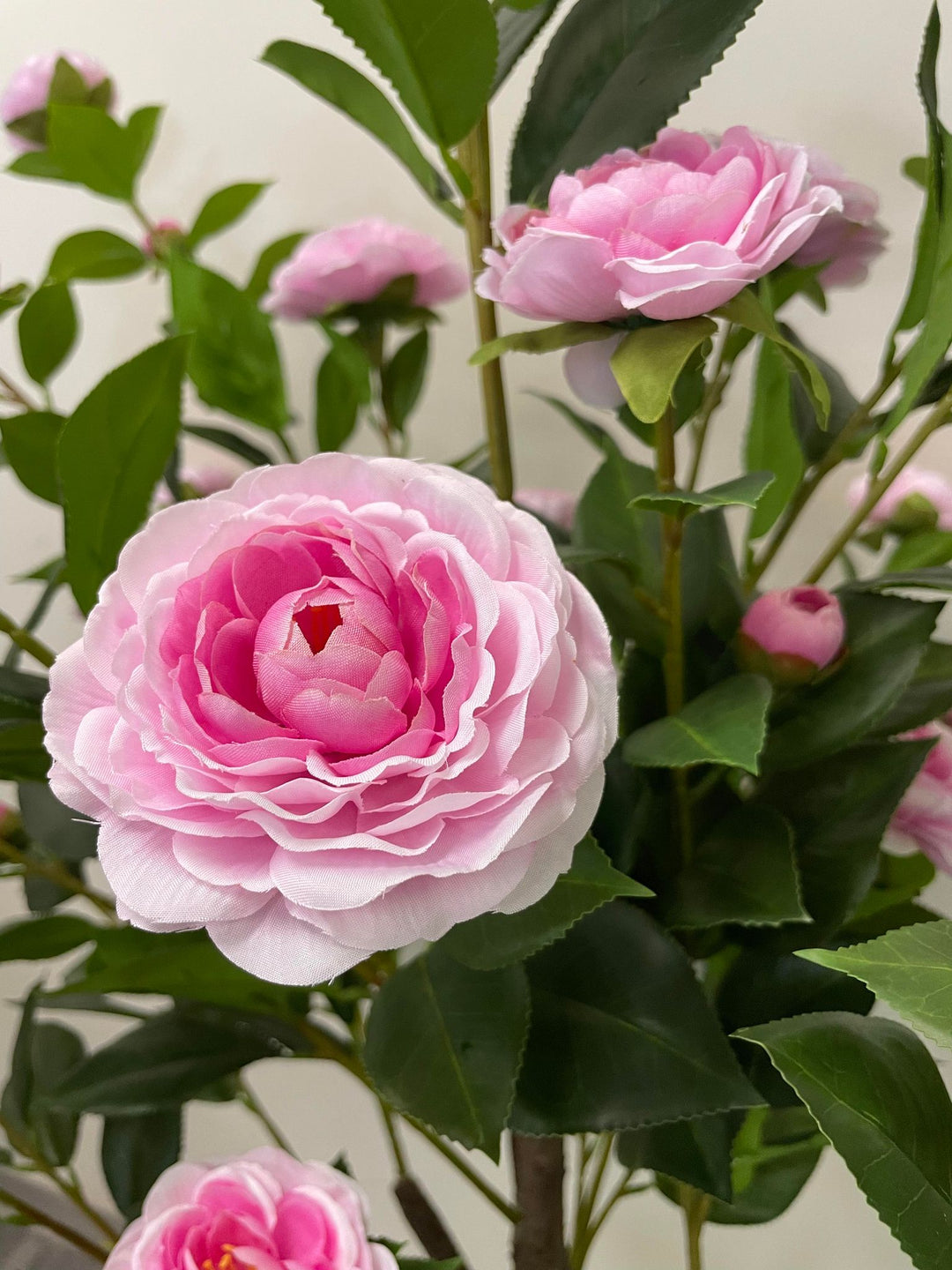 Close-up of a pink artificial flower with layered petals and green leaves, showcasing detailed craftsmanship, ideal for enhancing home or office décor with a touch of elegance