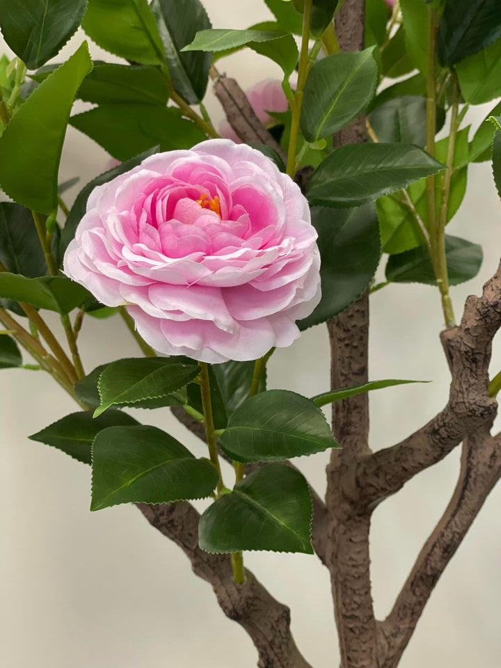 Close-up of a pink artificial flower with layered petals and green leaves, showcasing detailed craftsmanship, ideal for enhancing home or office décor with a touch of elegance
