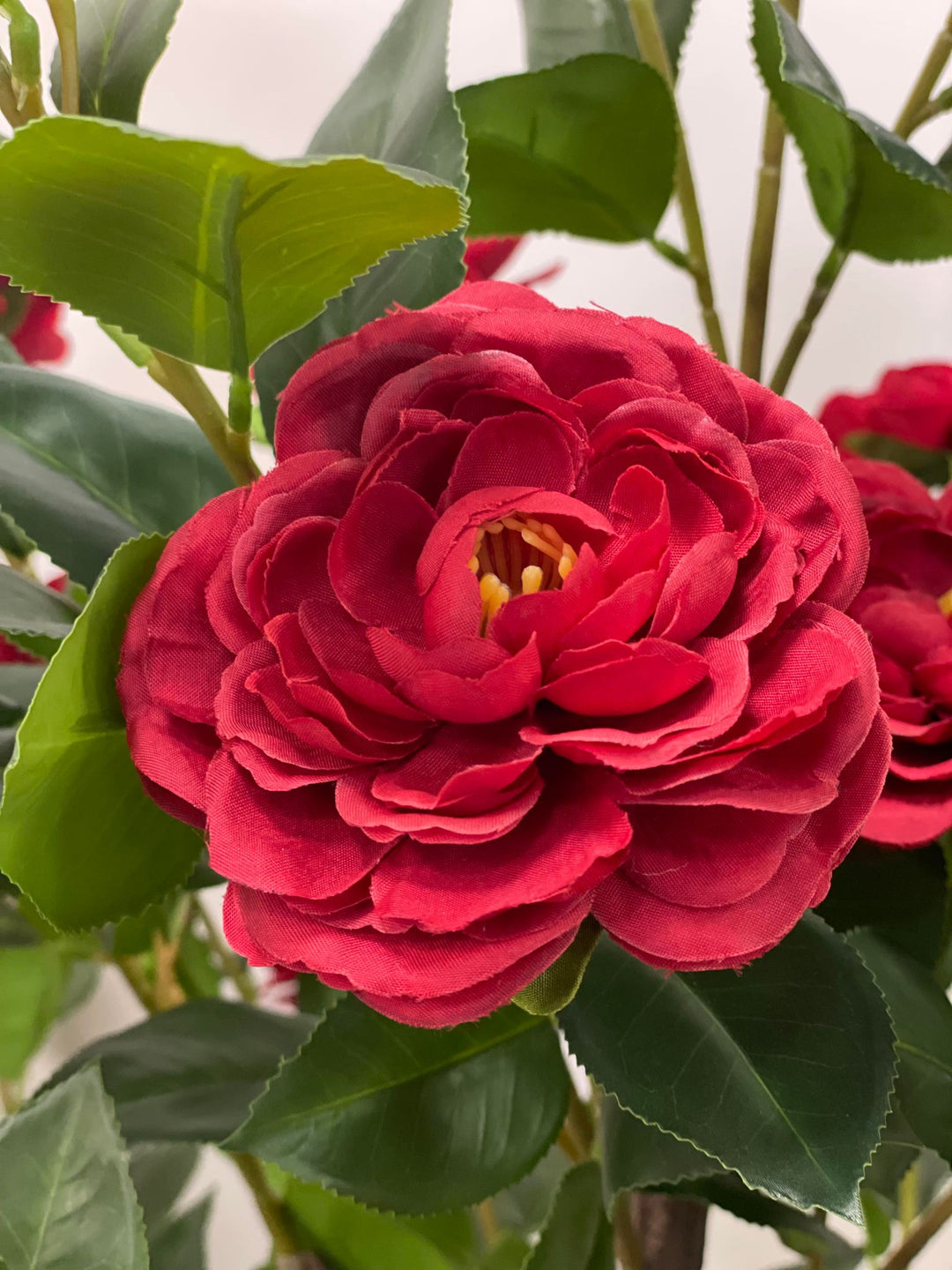 Close-up of a vibrant artificial red flower with detailed petals and lush green leaves, ideal for realistic floral arrangements in any setting.