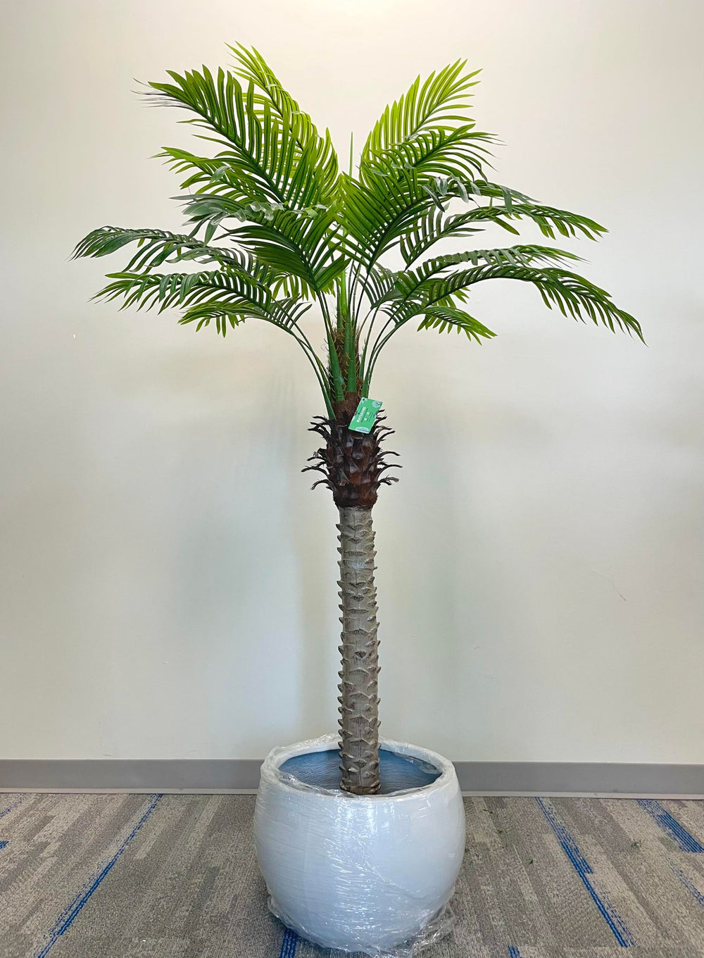 A realistic artificial palm tree placed in a white round planter, perfect for indoor spaces such as living rooms or offices, offering a tropical vibe.