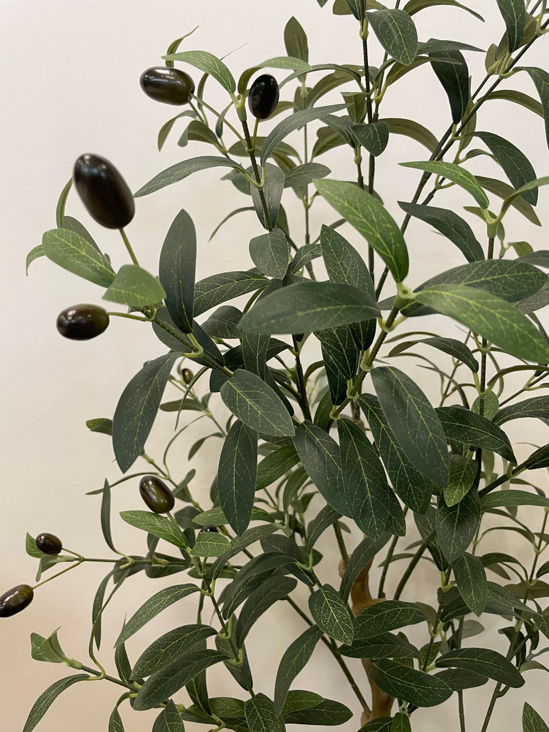 Close-up view of the artificial olive tree's leaves and small dark olives, showing the detailed texture and realistic design of the foliage against a neutral background