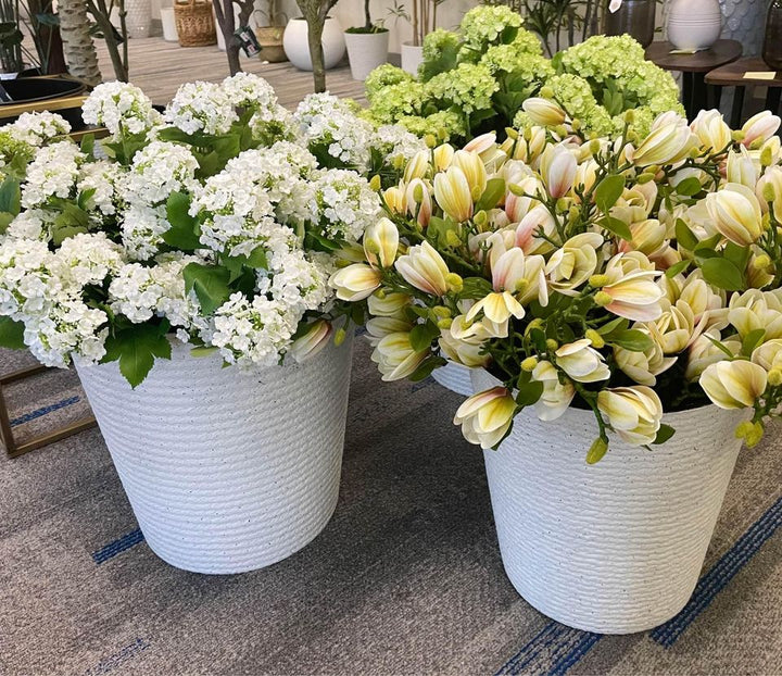 Two large planters filled with artificial flowers—white hydrangeas and cream magnolias with pink accents—placed on a modern rug. Common question: What are the best types of artificial flowers for home and office décor?"