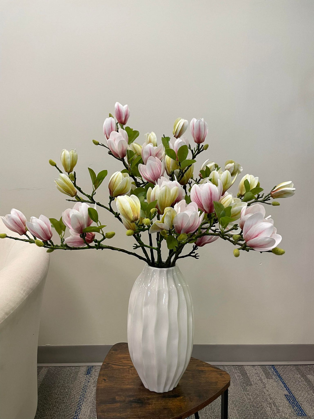 A stunning arrangement of artificial pink and cream magnolia flowers in a white ceramic vase. The realistic petals and vibrant green leaves create a refreshing and elegant floral display, perfect for brightening up any space in the home or office.