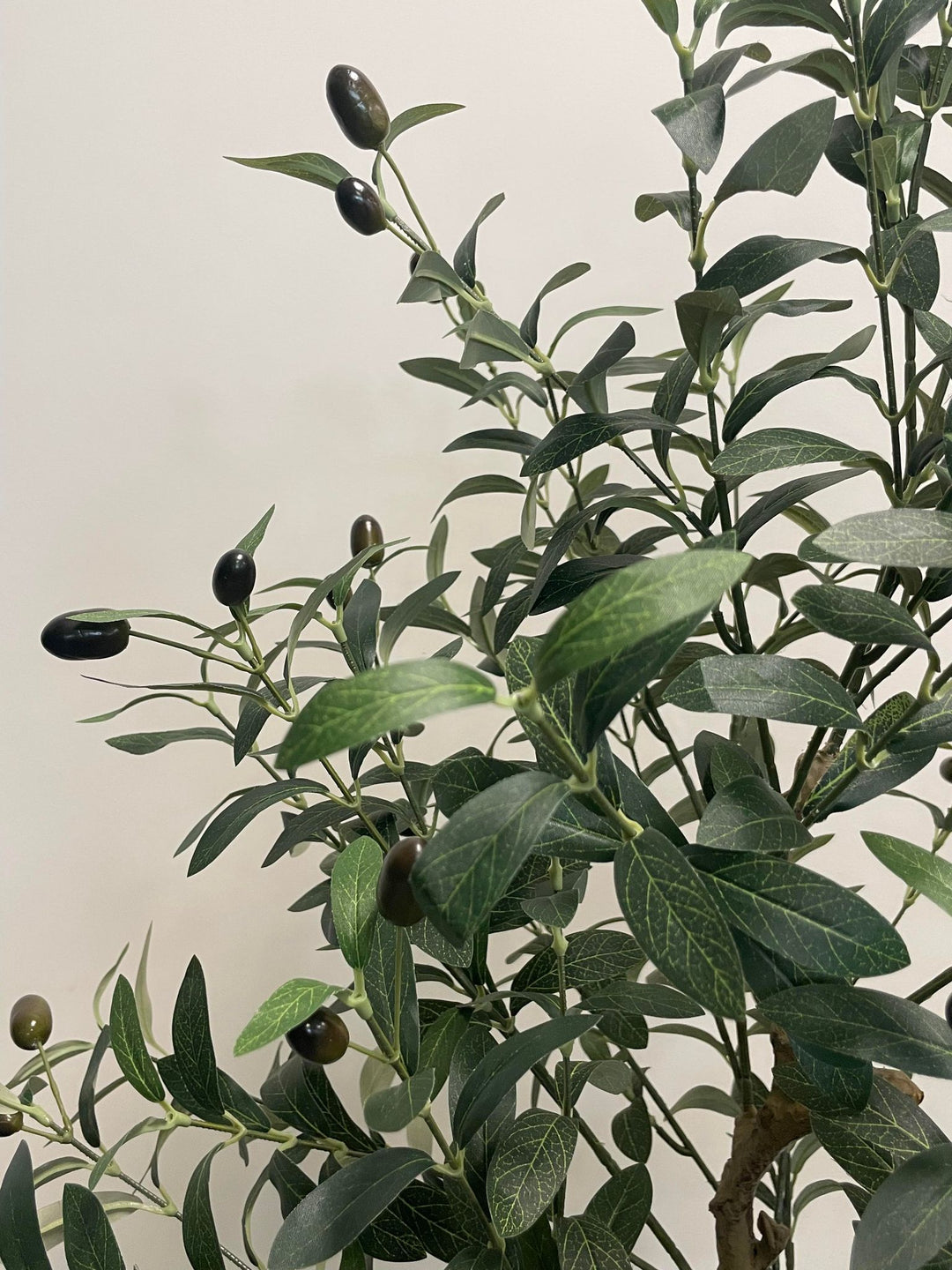 Close-up view of the artificial olive tree's leaves and small dark olives, showing the detailed texture and realistic design of the foliage against a neutral background.