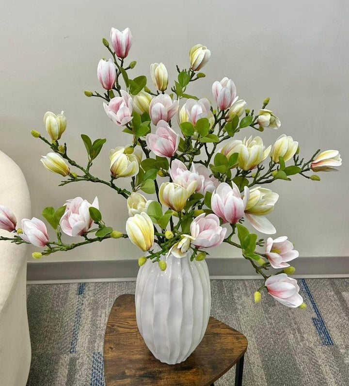 A stunning arrangement of artificial pink and cream magnolia flowers in a white ceramic vase. The realistic petals and vibrant green leaves create a refreshing and elegant floral display, perfect for brightening up any space in the home or office.