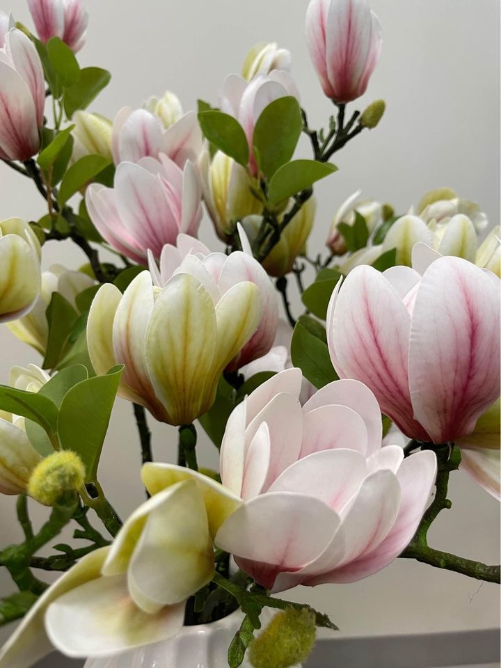 Close-up view of artificial magnolia flowers in shades of pink and cream with green leaves. Common question: Can artificial flowers be used as a long-lasting alternative to fresh flowers for home décor?
