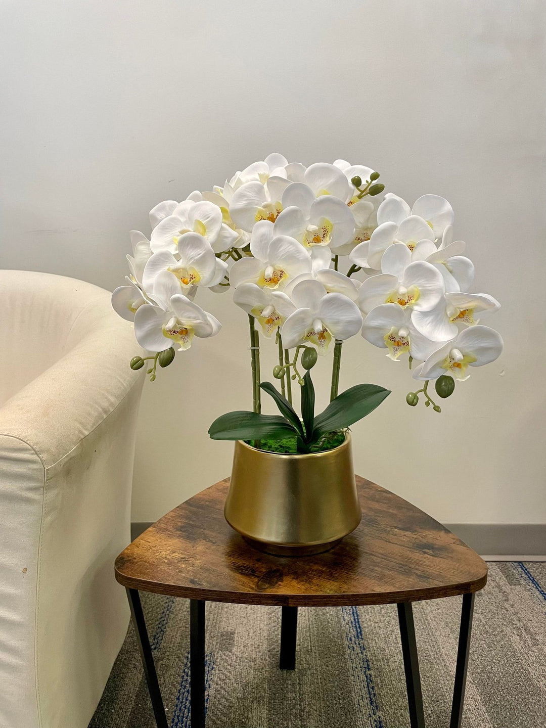 A stunning arrangement of white artificial orchids in a black ceramic planter on a wooden coffee table. Frequently asked question: What is the best way to care for artificial orchid flowers to keep them looking fresh?