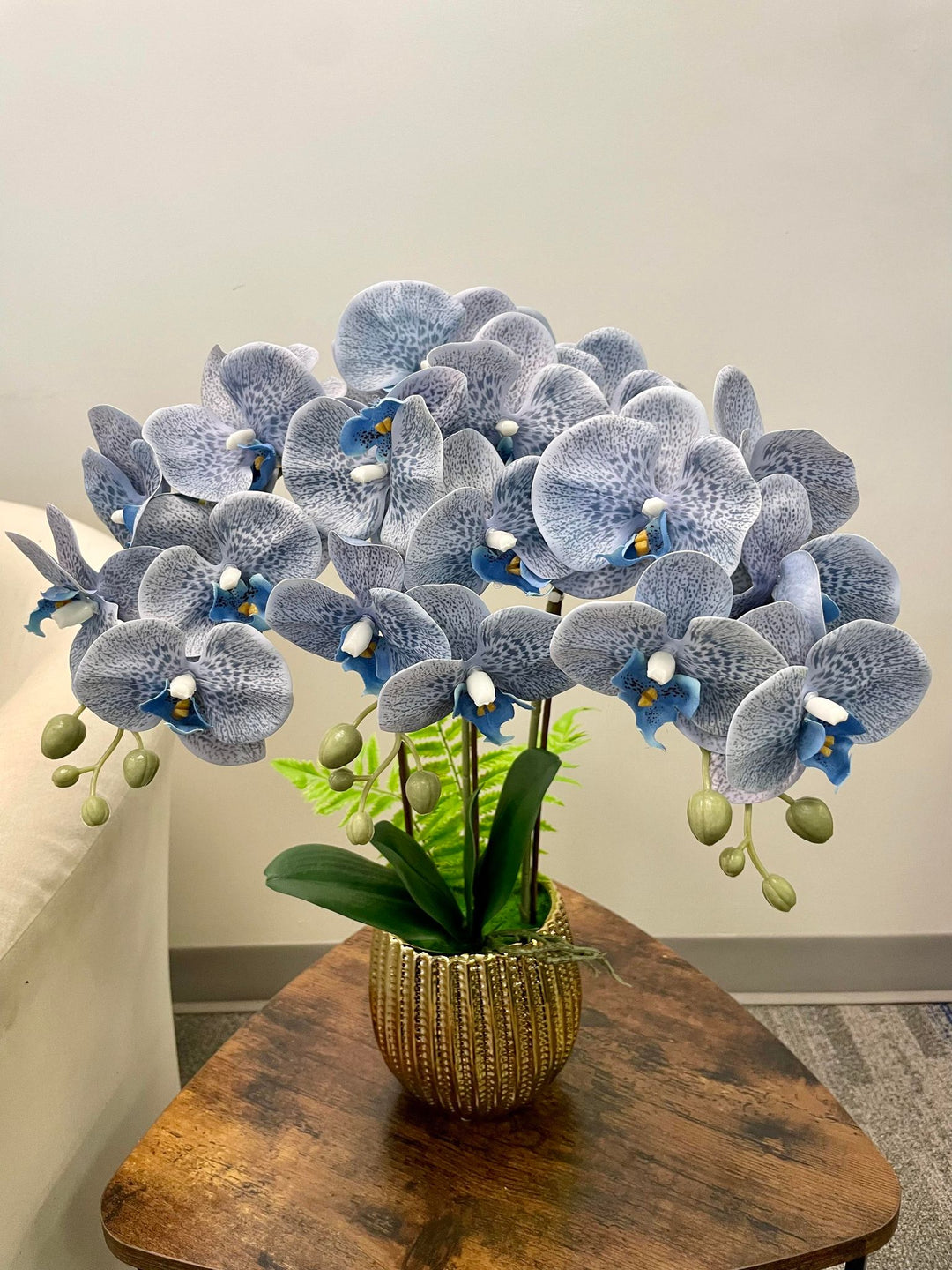 A vibrant arrangement of artificial blue orchids displayed in a golden textured planter on a wooden coffee table. Frequently asked question: Are artificial orchids better than real ones for long-lasting home decor?