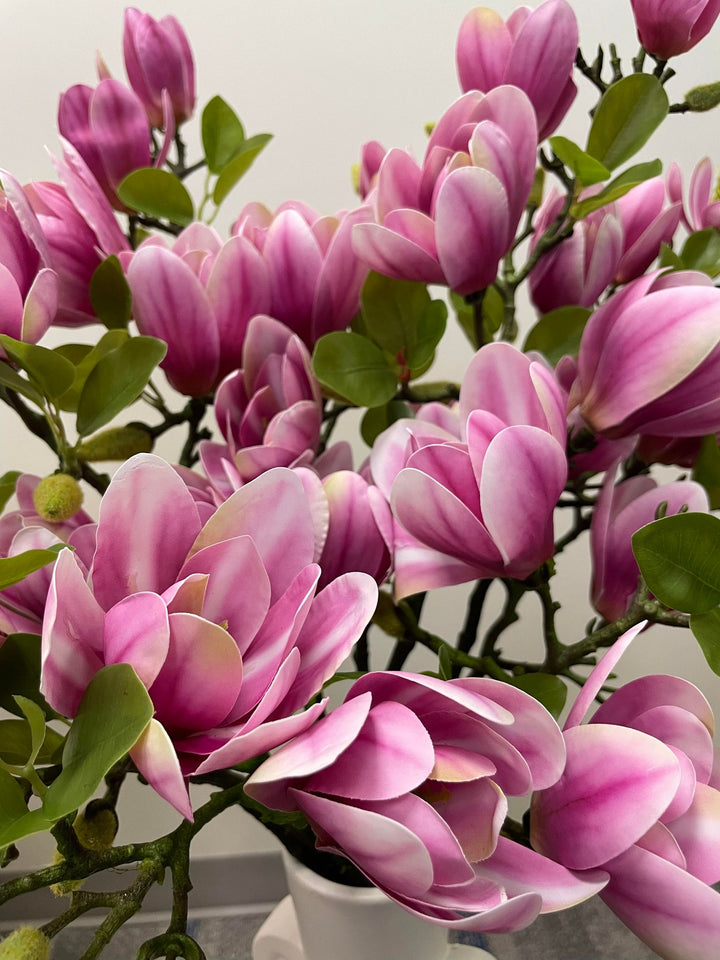 Close-up of a bouquet of artificial pink magnolia flowers with vibrant green leaves. The delicate petals of the flowers are intricately designed, providing a realistic and colorful touch to the arrangement, perfect for enhancing interior home decor.