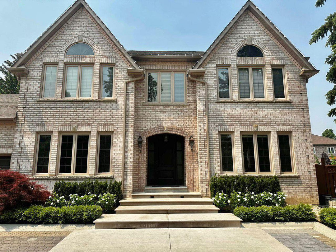 Front view of a large brick house with a manicured garden. The entrance features a set of steps surrounded by green shrubs and white flowering plants. What are the best landscaping tips to enhance curb appeal?