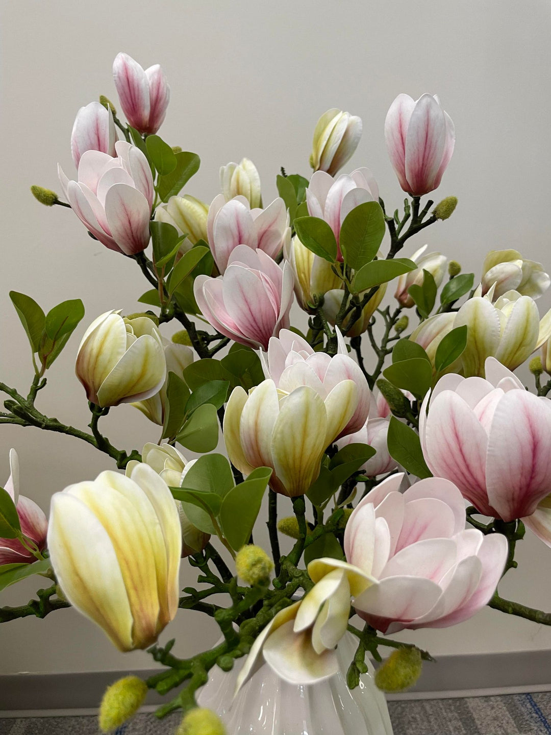 Close-up view of artificial magnolia flowers in shades of pink and cream with green leaves. Common question: Can artificial flowers be used as a long-lasting alternative to fresh flowers for home décor?