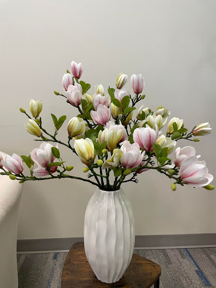 A stunning arrangement of artificial pink and cream magnolia flowers in a white ceramic vase. The realistic petals and vibrant green leaves create a refreshing and elegant floral display, perfect for brightening up any space in the home or office.