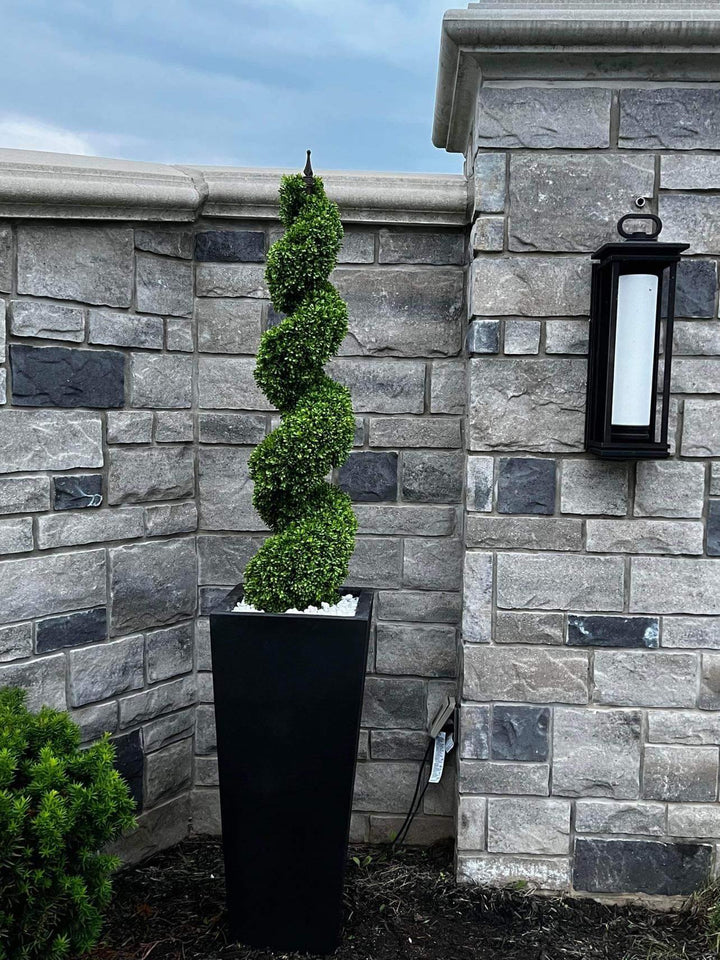 Artificial spiral topiary in a tall black planter, ideal for enhancing the elegance of outdoor landscapes or entranceways.