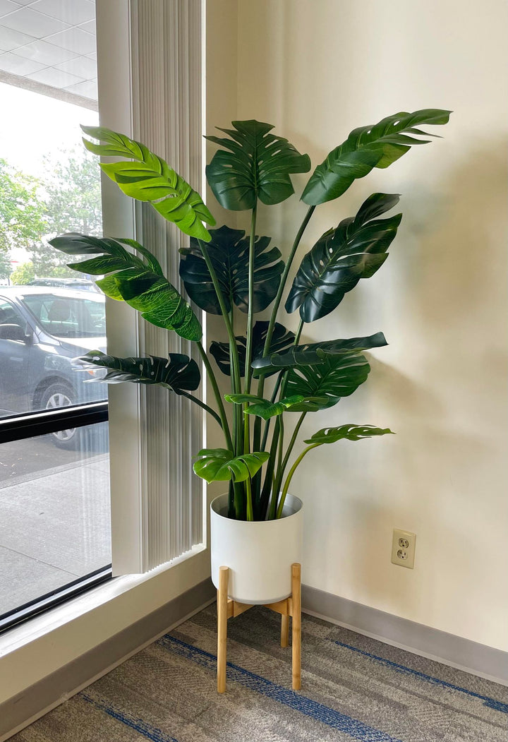 Large artificial monstera plant with vibrant green, split leaves, displayed in a sleek white pot on a wooden floor, enhancing the indoor decor with a tropical touch