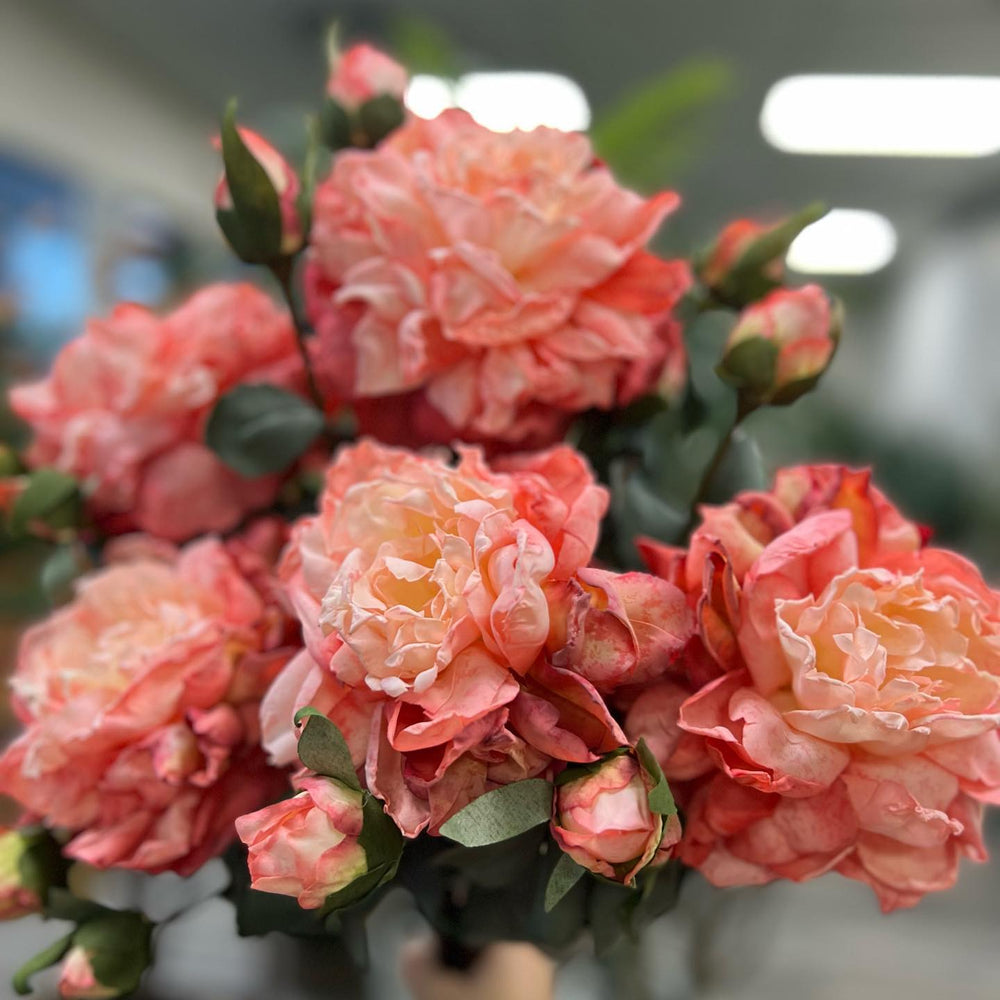 A bouquet of vibrant artificial roses in soft coral and peach tones, featuring lush, realistic petals and buds. This arrangement is ideal for enhancing home décor or creating a romantic floral display.