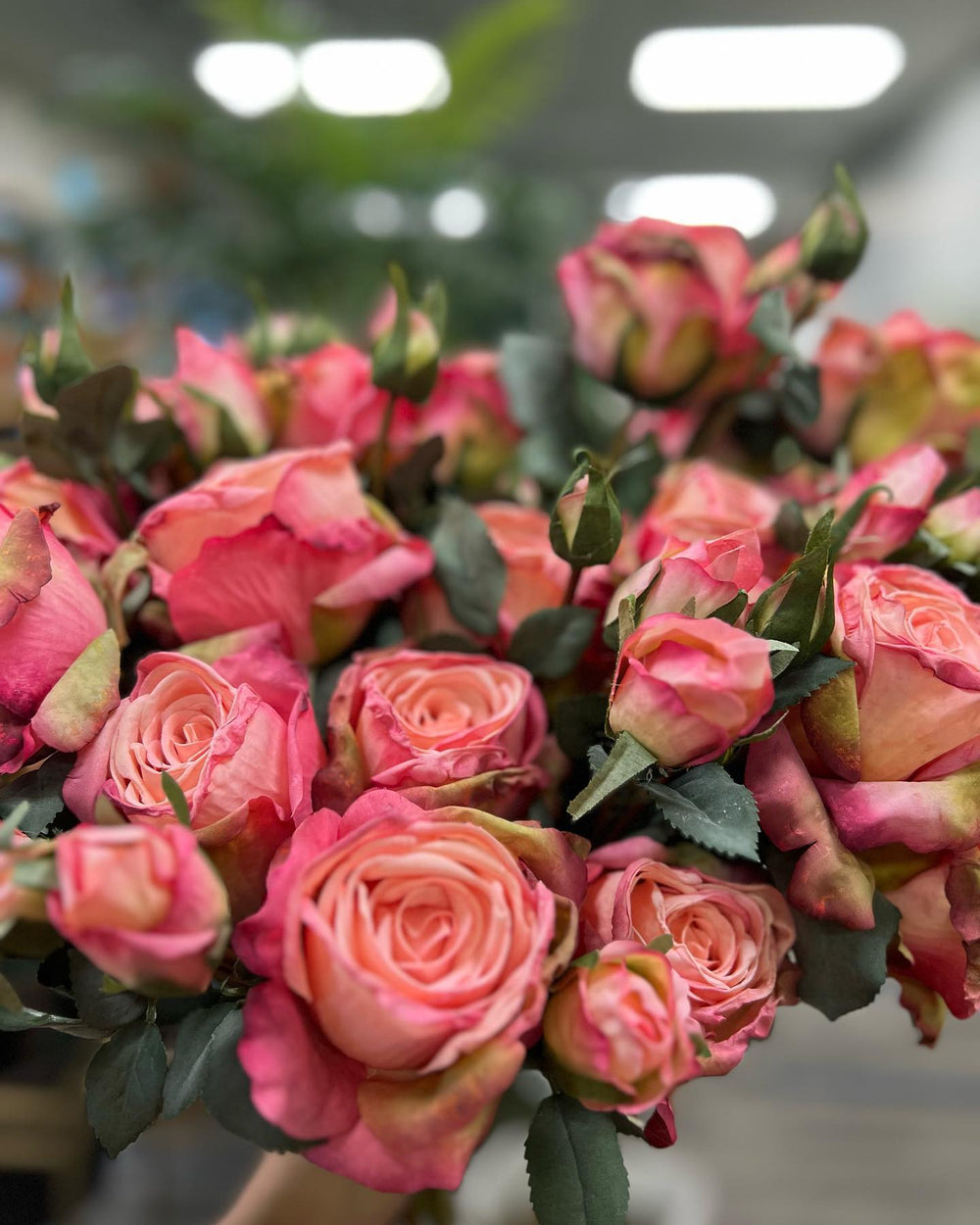 A vibrant bouquet of artificial roses with pink and peach hues, surrounded by green leaves. The intricate petals and rich colors make this floral arrangement a stunning display, perfect for home décor or special occasions.