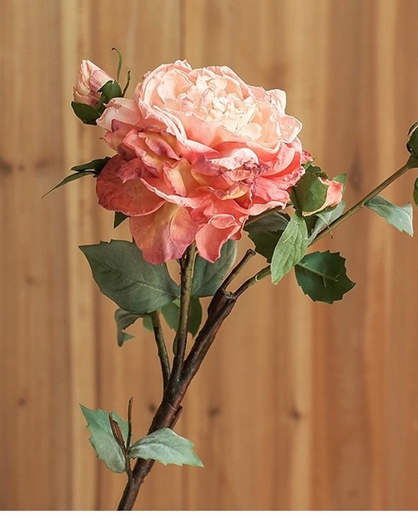 A close-up of a beautifully detailed artificial rose in soft pink and peach hues, with green leaves and a natural-looking stem. Perfect for home décor, floral arrangements, or adding elegance to any space.