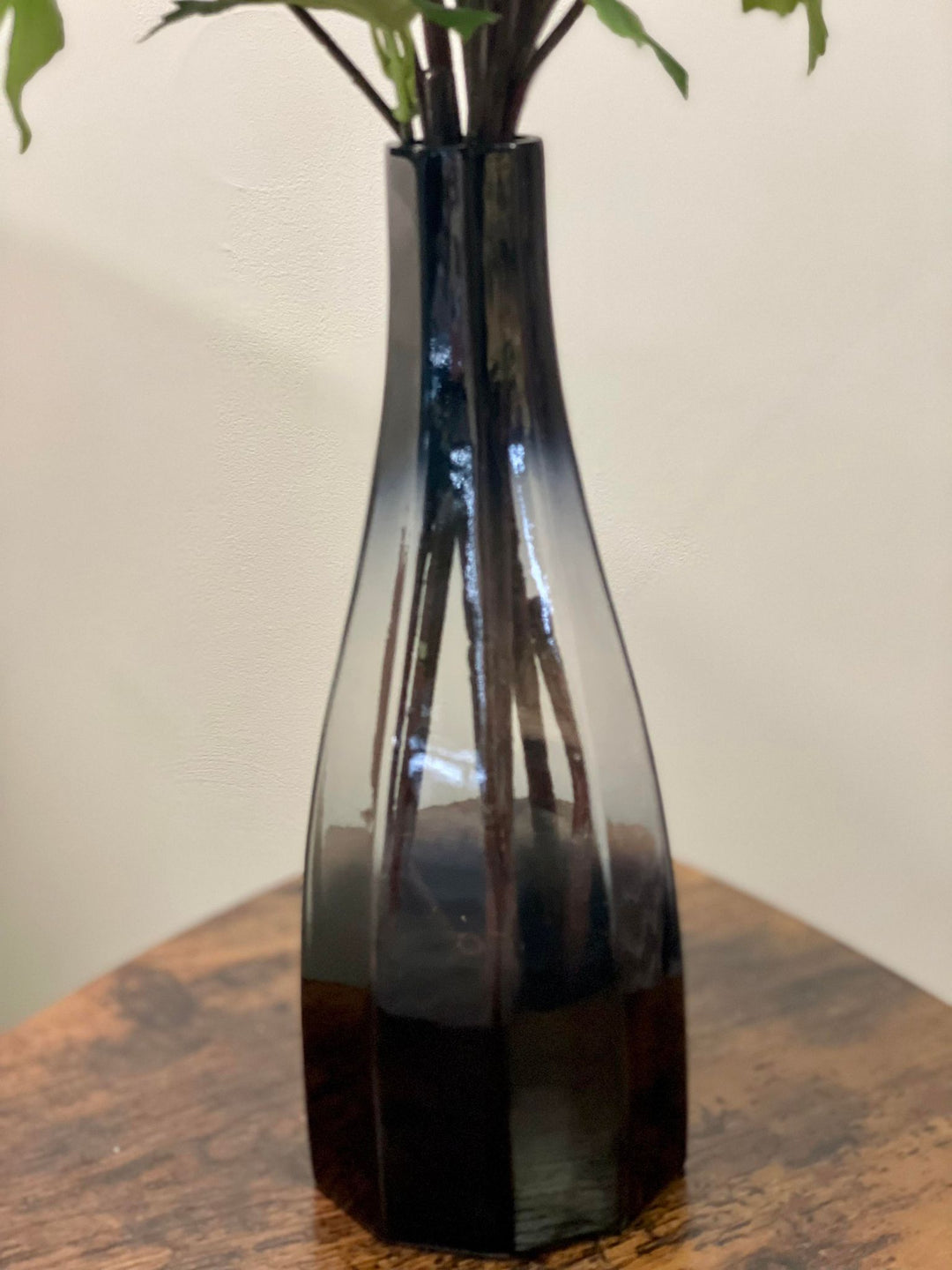 Close-up of a sleek black glass vase with a subtle gradient on a wooden coffee table. Frequently searched question: What is the best material for a vase to use with artificial flowers?