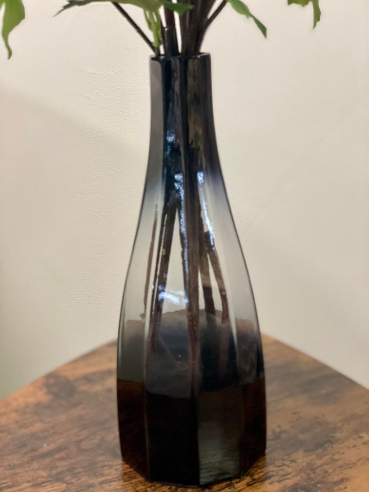 Close-up of a sleek black glass vase with a subtle gradient on a wooden coffee table. Frequently searched question: What is the best material for a vase to use with artificial flowers?