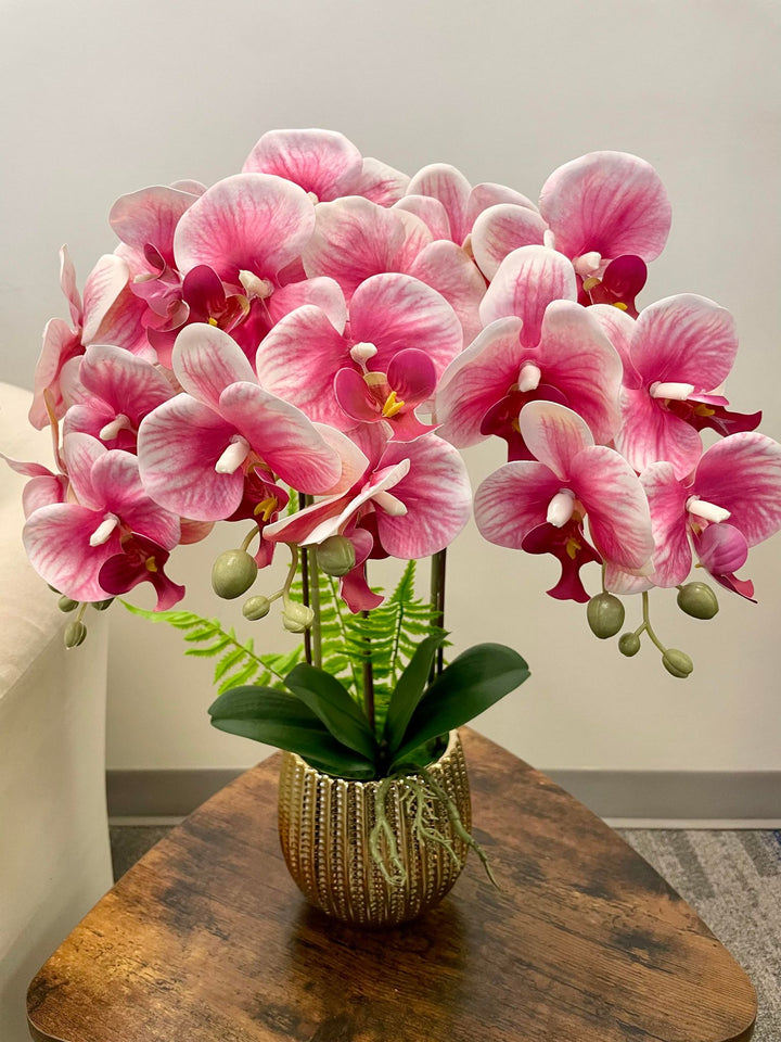 A stunning arrangement of pink and white artificial orchids in a gold textured pot, complete with lush green leaves and ferns. How can I ensure my artificial plants remain dust-free and vibrant?