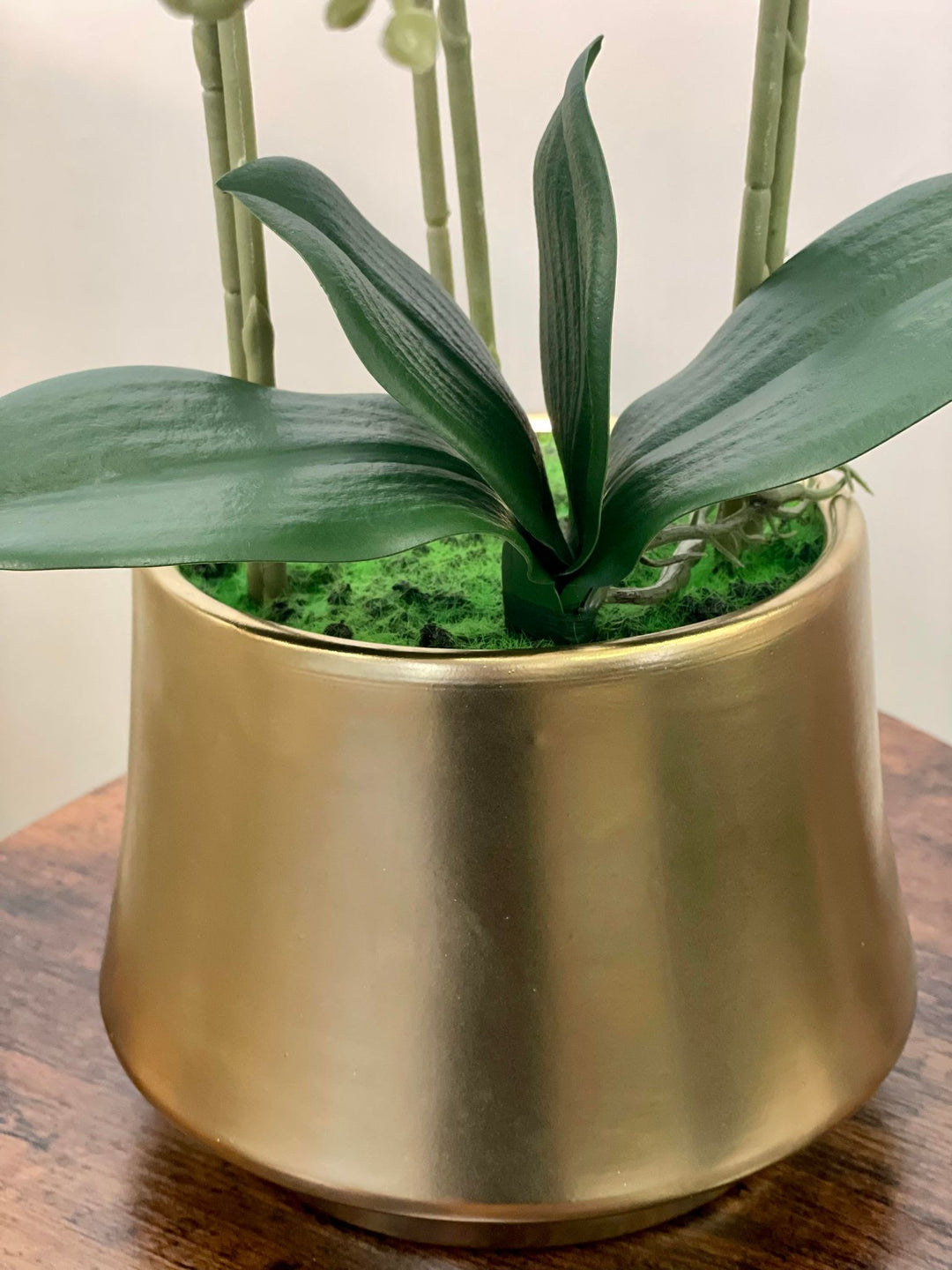 A close-up of a modern gold planter holding artificial orchid leaves, showcasing its sleek and elegant design. Frequently asked question: How do I select the right planter for artificial plants to complement home decor?