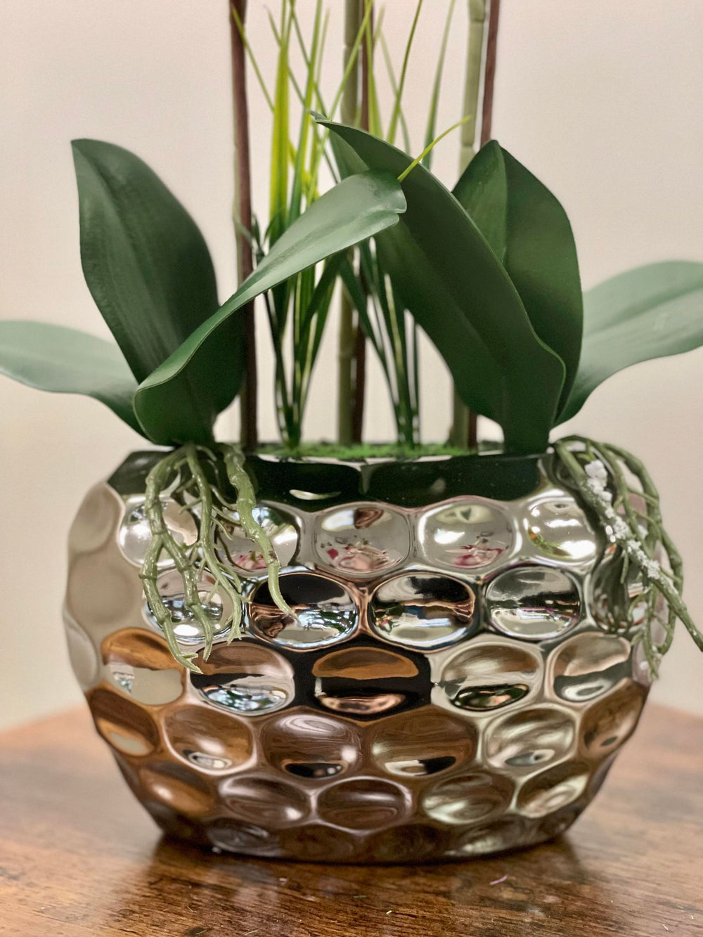 Close-up of a shiny silver planter holding artificial orchid leaves and stems with detailed texture. Frequently asked question: What type of pots or planters are best for displaying artificial plants indoors?