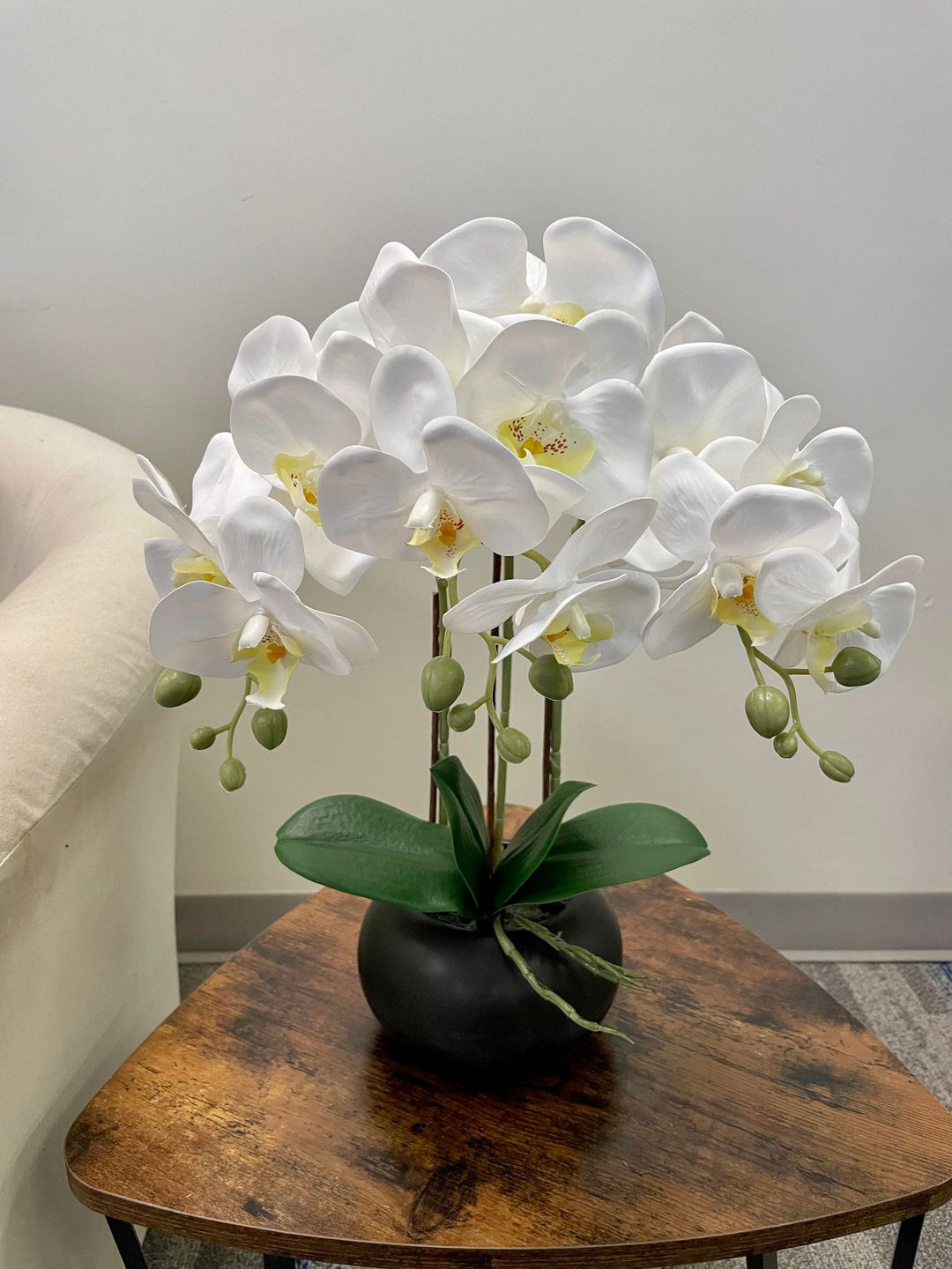 A stunning arrangement of white artificial orchids in a black ceramic planter on a wooden coffee table. Frequently asked question: What is the best way to care for artificial orchid flowers to keep them looking fresh?