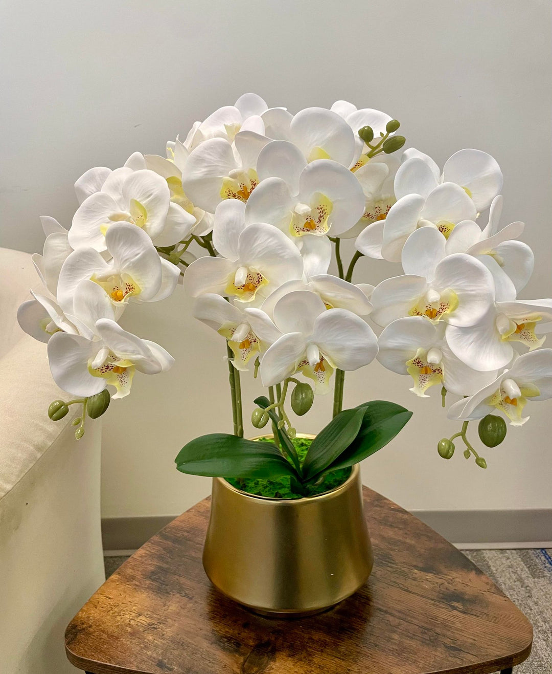 A stunning arrangement of white artificial orchids in a black ceramic planter on a wooden coffee table. Frequently asked question: What is the best way to care for artificial orchid flowers to keep them looking fresh?