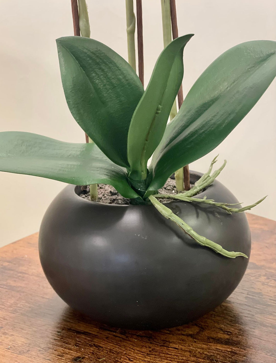 A modern black ceramic planter holding an artificial orchid with realistic green leaves, placed on a wooden table. Frequently asked question: What are the best types of planters for displaying artificial plants indoors?