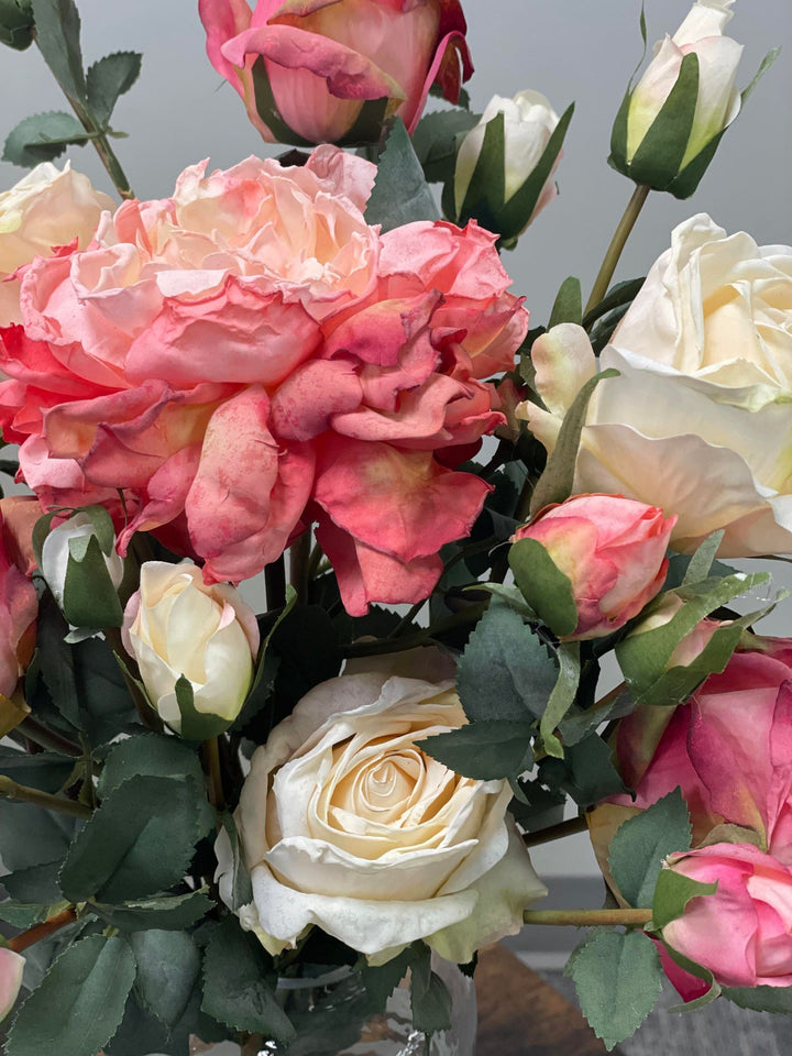 Close-up of artificial blush pink and cream roses with green leaves in a floral arrangement. Common question: Are artificial roses realistic and do they require maintenance?
