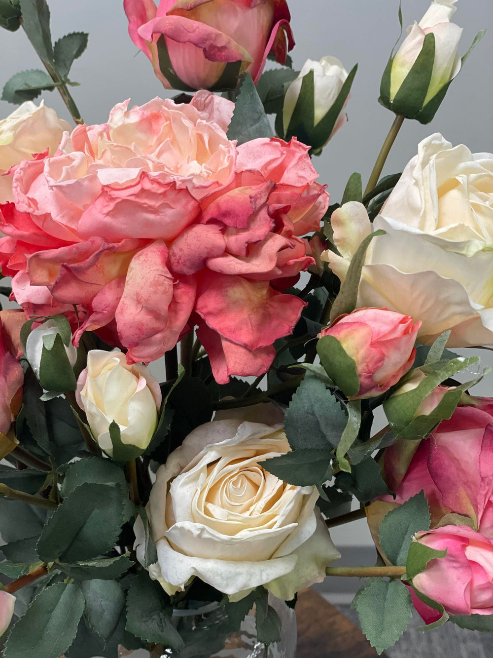 Close-up of a mixed artificial bouquet featuring cream, blush pink, and coral roses with green leaves. Popular search question: How to choose high-quality artificial flowers for a natural look?