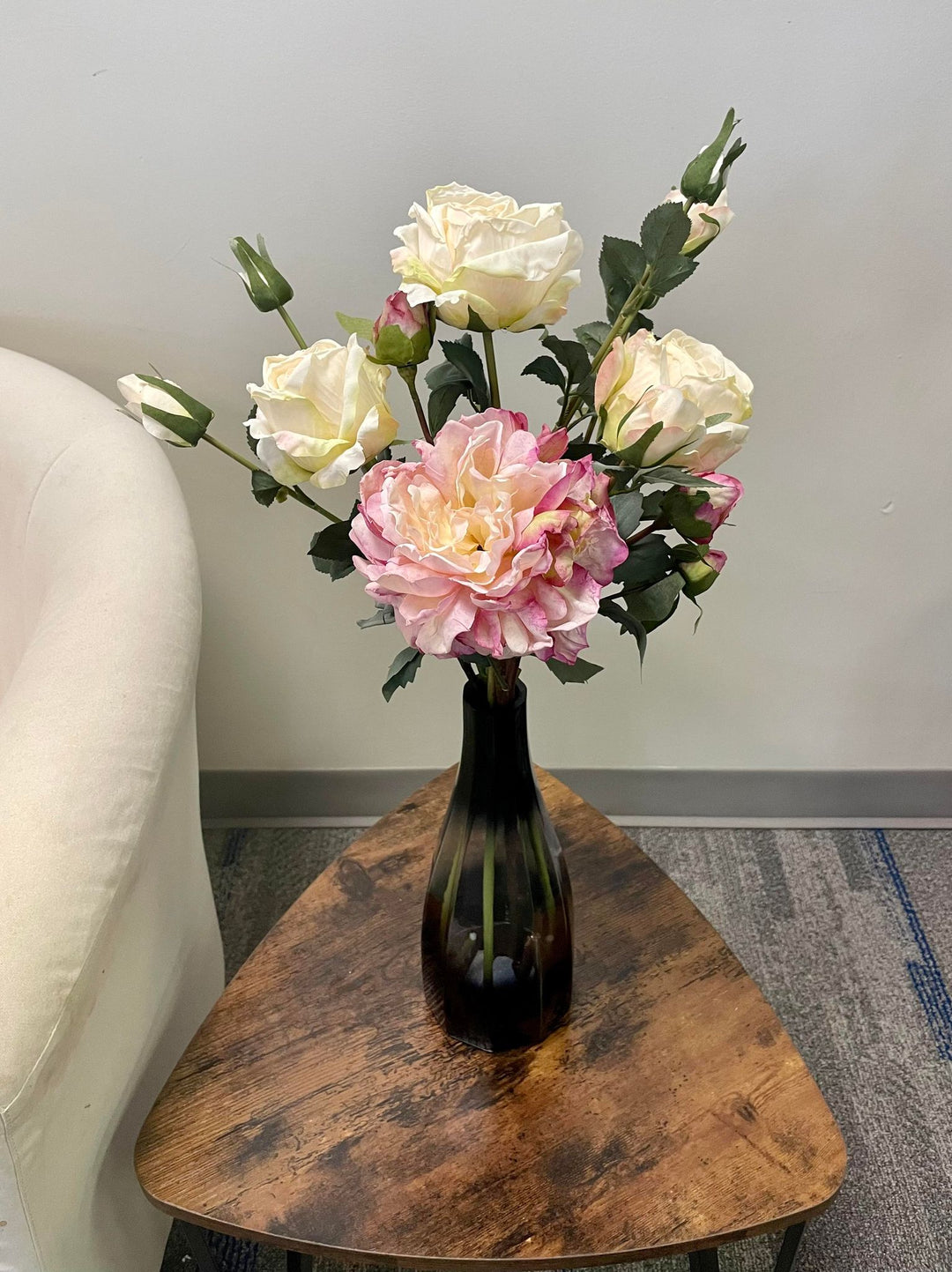 Artificial cream and blush-colored roses arranged in a tall black vase, placed on a wooden coffee table. Common question: How long do artificial flowers last and are they suitable for home decor?
