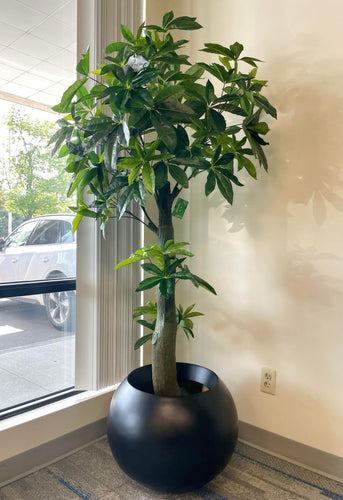 Artificial money tree with lush green leaves in a stylish white textured planter, placed beside a cozy white armchair in a modern indoor setting, perfect for enhancing office or home decor.